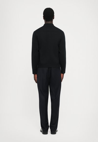 Sorte langærmede top med krave, parret med mørke bukser. Glat tekstur, tætsiddende design og minimalistisk look.