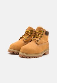 Botine scurte din suede bej, cu design cu șireturi, ochiuri metalice și căptușeală din blană moale. Talpa din cauciuc cu model oferă aderență și durabilitate.