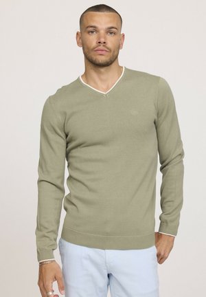 Pull-over en maille douce de couleur vert olive clair à col en V, avec un contraste de bord blanc au niveau de l'encolure et de la taille, et des manches ajustées.