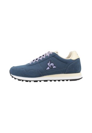 Zapatilla deportiva azul y beige con cordones morados, suela texturizada y un logo de pájaro en el lateral, vista desde el lado exterior.