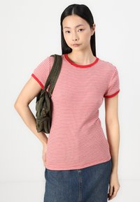 Rot-weißer gestreifter T-Shirt mit einem kontrastierenden roten Rippkragen und Ärmelbündchen, kombiniert mit einer grünen Cordtasche.