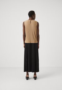 Beige plisserte ermeløs topp med detalj i form av nøkkelhull bak, kombinert med en lang svart plissert skjørt og svarte hælsandaler.