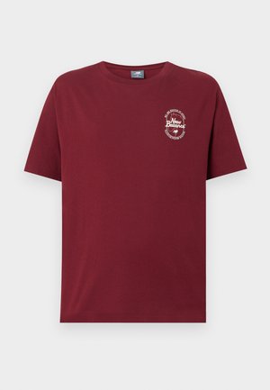 Tumši sarkana īsām piedurknēm T-krekls ar apaļu apkakli, ar nelielu balto New Balance logotipu un tekstu kreisajā krūtīs, kas vēsta "New Balance, Bostonas Masačūsetsā."