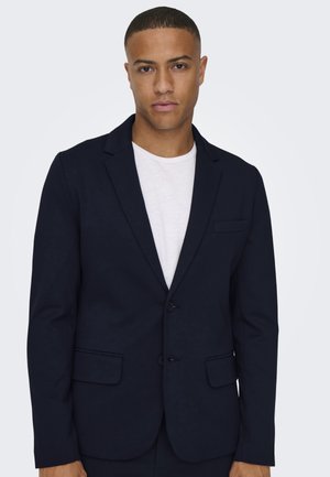 Marineblazer van een gladde stof, met één rij knopen en twee knopen. Heeft een notch-lapel, één borstzak en twee voorzakken.