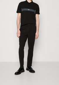 Černé polo tričko s šedým vodorovným pruhem a logem, doplněné o černé slim-fit kalhoty a lesklé černé polobotky na šněrování.