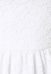White lace fabric with intricate floral patterns. Ruffled hem at the bottom creates texture. Soft, lightweight material.