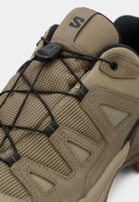 Ανοιχτό καφέ παπούτσι εξωτερικού χώρου με υλικά από δίχτυ και σουέντ. Διαθέτει ασφαλές σύστημα κορδονιών με μαύρο κουμπί. Τριγωνικές εγκοπές κατά μήκος των πλευρών.