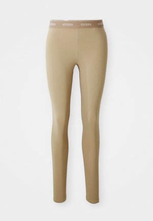 Leggings aderenti beige con cintura elastica marchiata "GUESS", esposti piatti su uno sfondo bianco.
