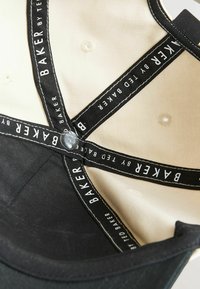 Vue intérieure d'une casquette noire et beige avec une bande en tissu noir portant l'inscription "BAKER BY TED BAKER" croisée au centre.