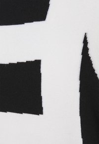Gros plan sur un tissu avec un motif géométrique noir et blanc composé de formes rectangulaires aux bords nets.