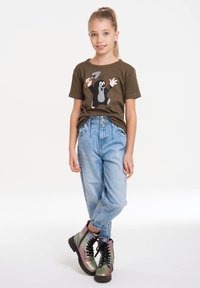 Camiseta de algodón verde con un gráfico de un topo de dibujos animados, combinada con unos vaqueros de cintura alta de color azul claro y botas de cordones iridiscentes.
