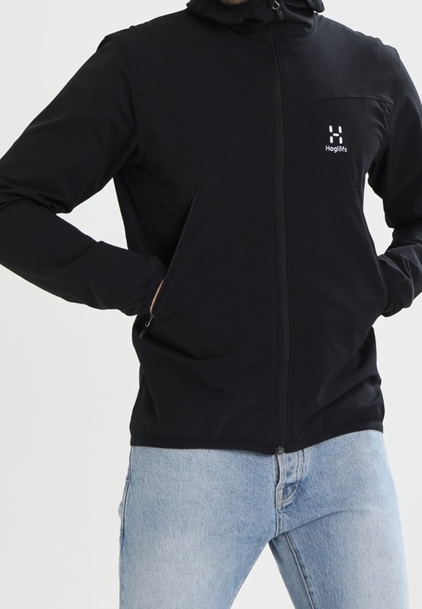 Veste noire à fermeture éclair avec capuche, fabriquée en tissu doux, avec un panneau cousu sur la poitrine et des poches latérales. Logo sur le côté gauche.