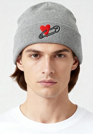 Gray knit beanie featuring a red heart and black safety pin embroidery. The textured fabric has a ribbed design that contours snugly.