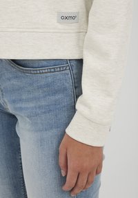 Lys grå sweatshirt med OXMO-label; hyggelig tekstur. Sammen med blå denim jeans, der viser en tætsiddende pasform og subtle falmede design.