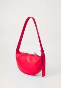 Red leather shoulder bag with a curved shape, adjustable strap, and zippered closure. Smooth texture with minimal hardware accents.