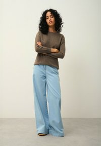 Brun strukturerad tröja med långa ärmar i kombination med ljusblå vida jeans. Båda plaggen har avslappnad passform och en casual design.