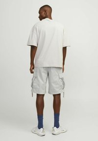 Lys grå cargo shorts med store sidelommer, parret med en løstsiddende hvid t-shirt. Komplementer inkluderer blå strømper og hvide sneakers.