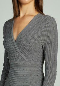 Rochie gri cu mânecă lungă și decolteu adânc în formă de V, cu textură ribbed și accente metalice dispersate pe întreaga țesătură.