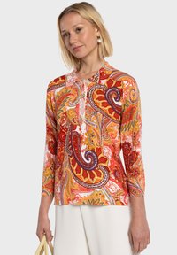 Haut à manches longues à motifs cachemire multicolores dans des tons rouges, orange et jaune, avec un col rond et des motifs complexes. Texture plate, coupe décontractée.