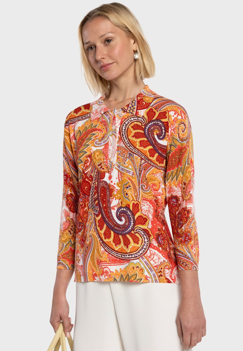 Haut à manches longues à motifs cachemire multicolores dans des tons rouges, orange et jaune, avec un col rond et des motifs complexes. Texture plate, coupe décontractée.