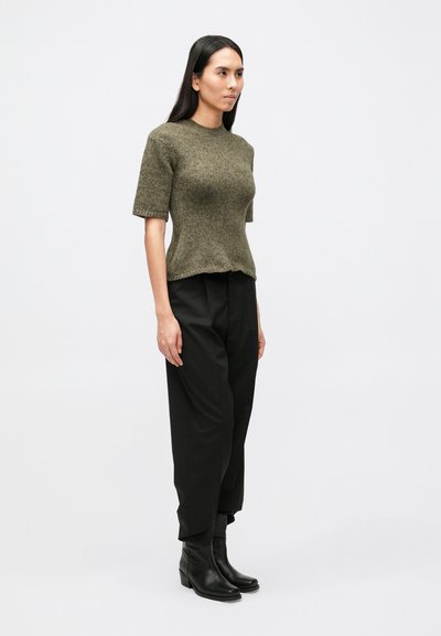 Olívovo zelený pletený krátky rukáv s okrúhlym výstrihom, kombinovaný s voľnými čiernymi nohavicami a čiernymi členkovými čižmami, na jednoduchom pozadí.