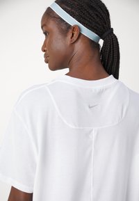 T-shirt branco da Nike com decote redondo, mangas curtas e um logotipo cinza discreto nas costas. Tecido de algodão suave com um corte descontraído.