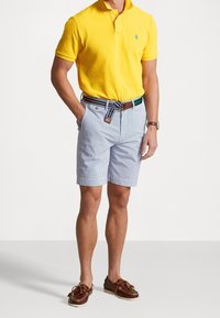 Gul polo-shirt, randiga blå shorts, bruna läderskonor för båt och ett flerfärgat bälte med bruna detaljer.