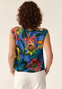 Blusa a maniche corte con sfondo blu caratterizzata da motivi floreali colorati in rosso, giallo e verde. Tessuto leggero con una vestibilità comoda.