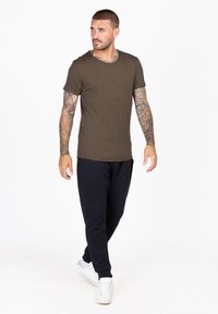 T-shirt in cotone verde oliva con scollo rotondo, abbinato a pantaloni jogger neri e sneakers bianche. Caratterizzato da una vestibilità slim e maniche corte.