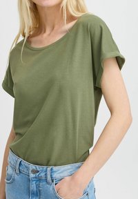 Camiseta de manga corta en verde oliva con un escote ancho y un corte relajado, combinada con unos vaqueros de tiro alto en azul claro. Textura suave.