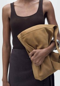 Rippenbraunes Tanktop, hochgeschnittener dunkelherbstrock und eine große, beige Tasche mit weicher Textur und silbernem Beschlag, die in einer Hand gehalten wird.