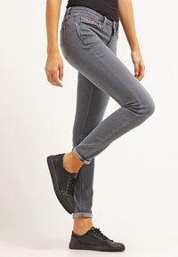 Jeans grises con un corte ajustado y largo hasta el tobillo, que cuentan con cinco bolsillos y costuras en contraste. Combinados con zapatillas negras de cordones.