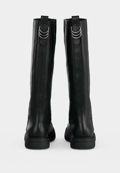 Paire de bottes hautes en cuir noir avec semelles épaisses et trois anneaux argentés sur les languettes à l'arrière.