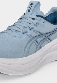 Ανοιχτό μπλε αθλητικό παπούτσι Asics με γκρι ρίγες λογότυπου, διχτυωτό επάνω μέρος, επενδυμένο κολάρο αστραγάλου και παχύ άσπρο απορροφητικό πέλμα.