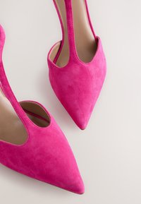 Élénk rózsaszín velúr magassarkú cipők hegyes orral és kivágott oldalakkal, sima belső béléssel és finom varrási részletekkel.