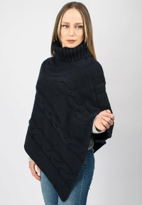 Marinblå kabelstickad poncho med hög ribbad krage, som visar ett strukturerat mönster och en lös, oversized design. Perfekt för lager-på-lager.