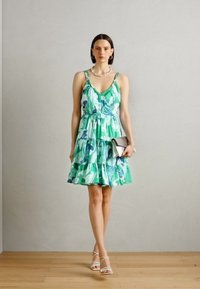 Robe florale verte et bleue avec une jupe à volants, des bretelles spaghetti et un corsage ajusté, assortie à une pochette argentée et des sandales à lanières.