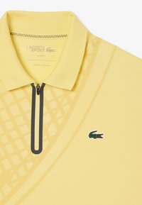 Polo giallo con colletto zip, design slim fit. Presenta un motivo testurizzato e un logo coccodrillo ricamato verde sul petto.