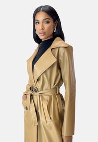 Light brown faux leather trench coat with a belted waist, large lapels, and button accents. Smooth texture with a tailored fit.