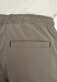 Elastic waistband pants in muted olive fabric with a smooth texture. Features a single welt pocket with black stitching detail.