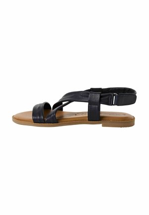 Flache Sandalen aus schwarzem Leder mit überkreuzten Riemen und einem Knöcherngurt. Sie verfügen über eine braune Gummisohle und eine glatte Textur.