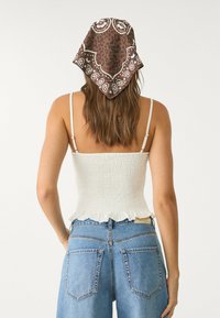 Canottiera bianca con arricciature e bordo a volant, abbinata a jeans in denim blu a vita alta. Bandana marrone a fantasia legata dietro.