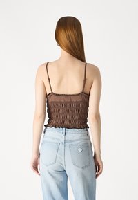 Brown smocked crop top with thin straps, textured fabric, and ruffled hem, paired with light blue high-waisted jeans with back pockets.