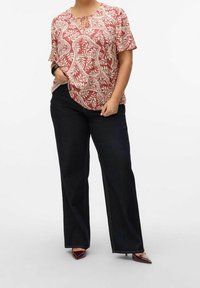 Blusa roja con estampado floral, de mangas cortas y con escote anudado, combinada con vaqueros de pierna ancha en azul oscuro y tacones puntiagudos burdeos.