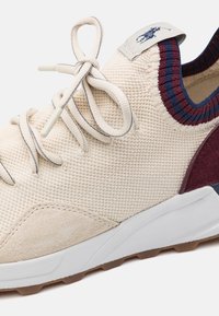 Beiga stickade sneakers med en strukturerad yta, med vinröda och marinblå accenter, en mockapanel och vit gummisula med brunt mönster.