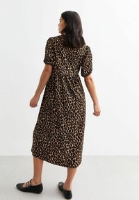Robe midi à imprimé léopard en tissu doux, avec des manches courtes bouffantes et une taille cintrée, présentée sur un mannequin portant des ballerines noires.
