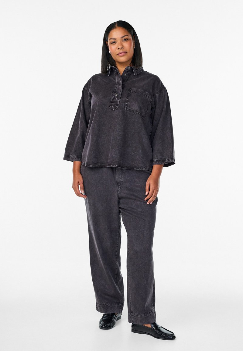 Schwarzes Oversize-Hemd aus Denim mit einer Tasche, kombiniert mit passenden locker sitzenden Hosen, die eine matte Textur und dezente Nähte aufweisen.