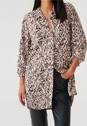 Chemisier à col avec un motif floral en noir, crème et pêche. Fabriqué en tissu doux, il présente des manches longues retroussées et une fermeture à boutons.