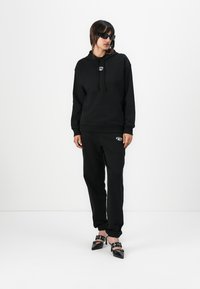 Black hooded sweatshirt with a logo, paired with matching black sweatpants. The outfit features a relaxed fit and soft texture. Accented with black sunglasses and stylish black shoes.