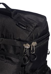 Czarny nylonowy plecak z teksturowaną powierzchnią, podwójnymi zamkami błyskawicznymi, akcentami z taśmy i uchwytem u góry ułatwiającym noszenie.